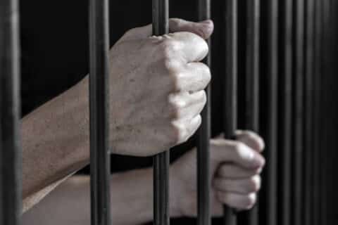 Les mains d'un prisonnier agrippant les barreaux d'une cellule en prison