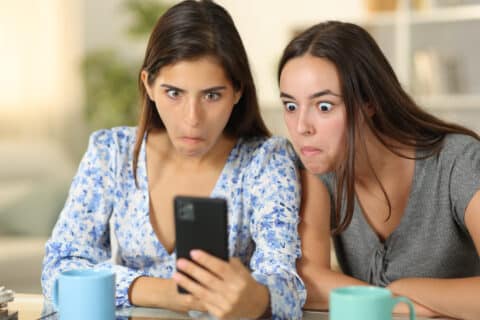 Femmes perplexes regardant leur téléphone portable à la maison