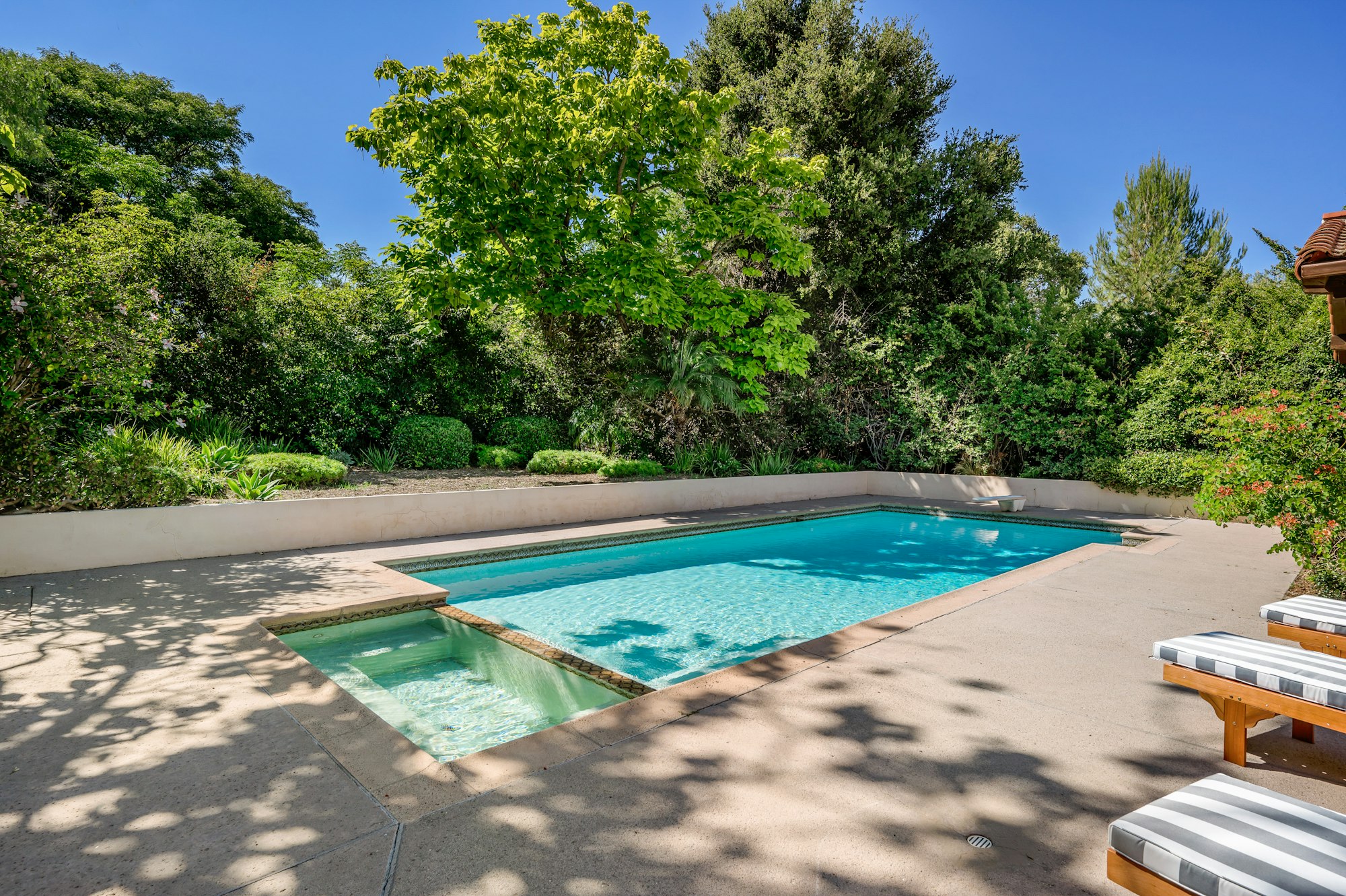an outdoor pool with two chairs near it and a fence surrounding