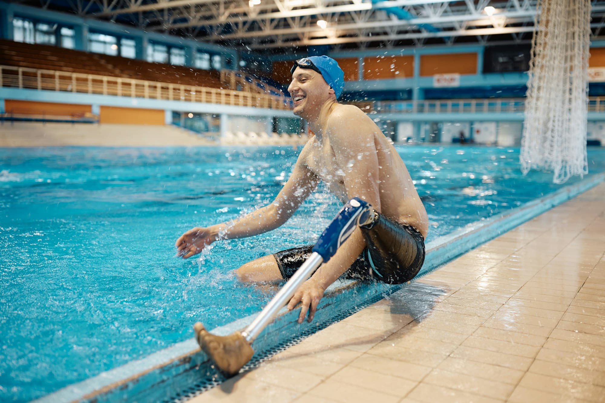 Athlete with a prosthetic leg having fun while splashing water by the edge of swimming pool.
