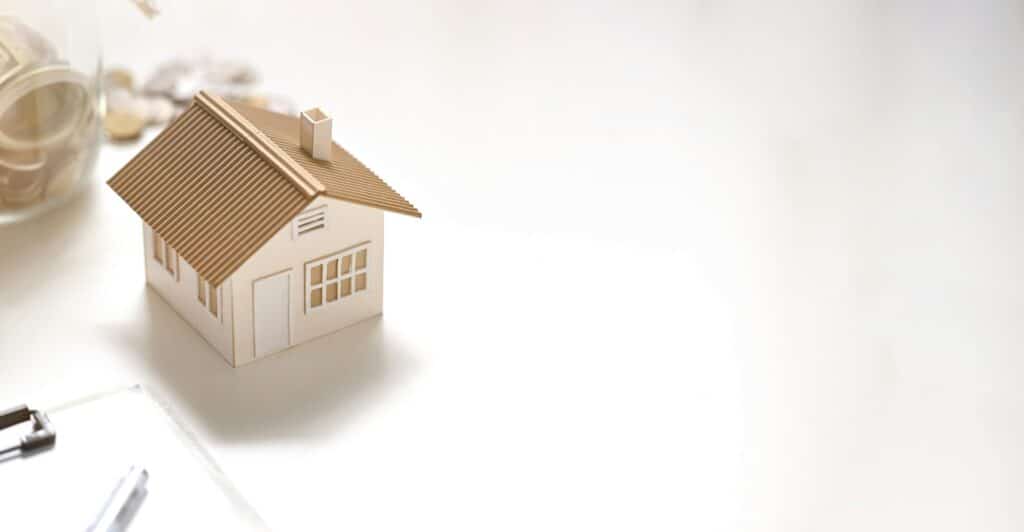 Photo of house model, clipboard, saving money in vase putting together on white table.