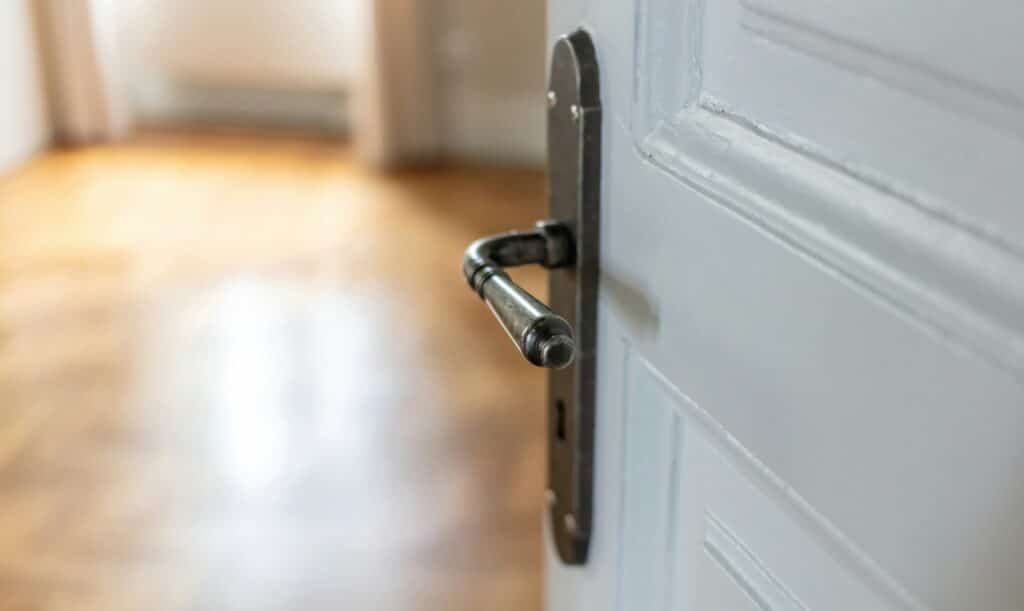 Door open close up. Retro doorknob on white door, blur floor parquet, classy room interior