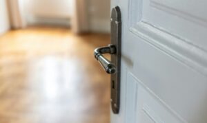 Door open close up. Retro doorknob on white door, blur floor parquet, classy room interior