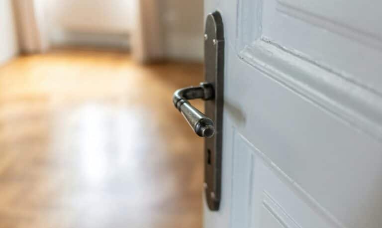 Door open close up. Retro doorknob on white door, blur floor parquet, classy room interior